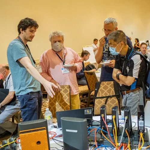 Masked participants gathered around a table of network equipment and cables