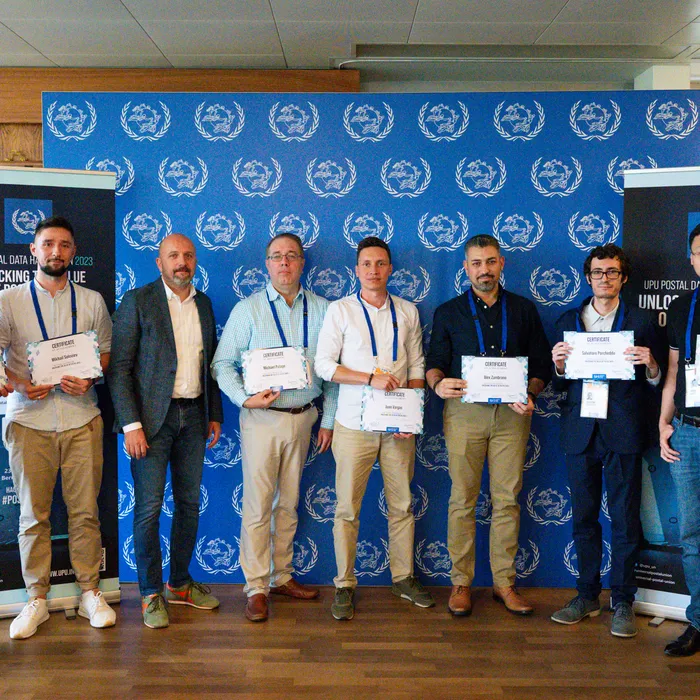 Hackathon participants holding their certificates in front of a UPU backdrop