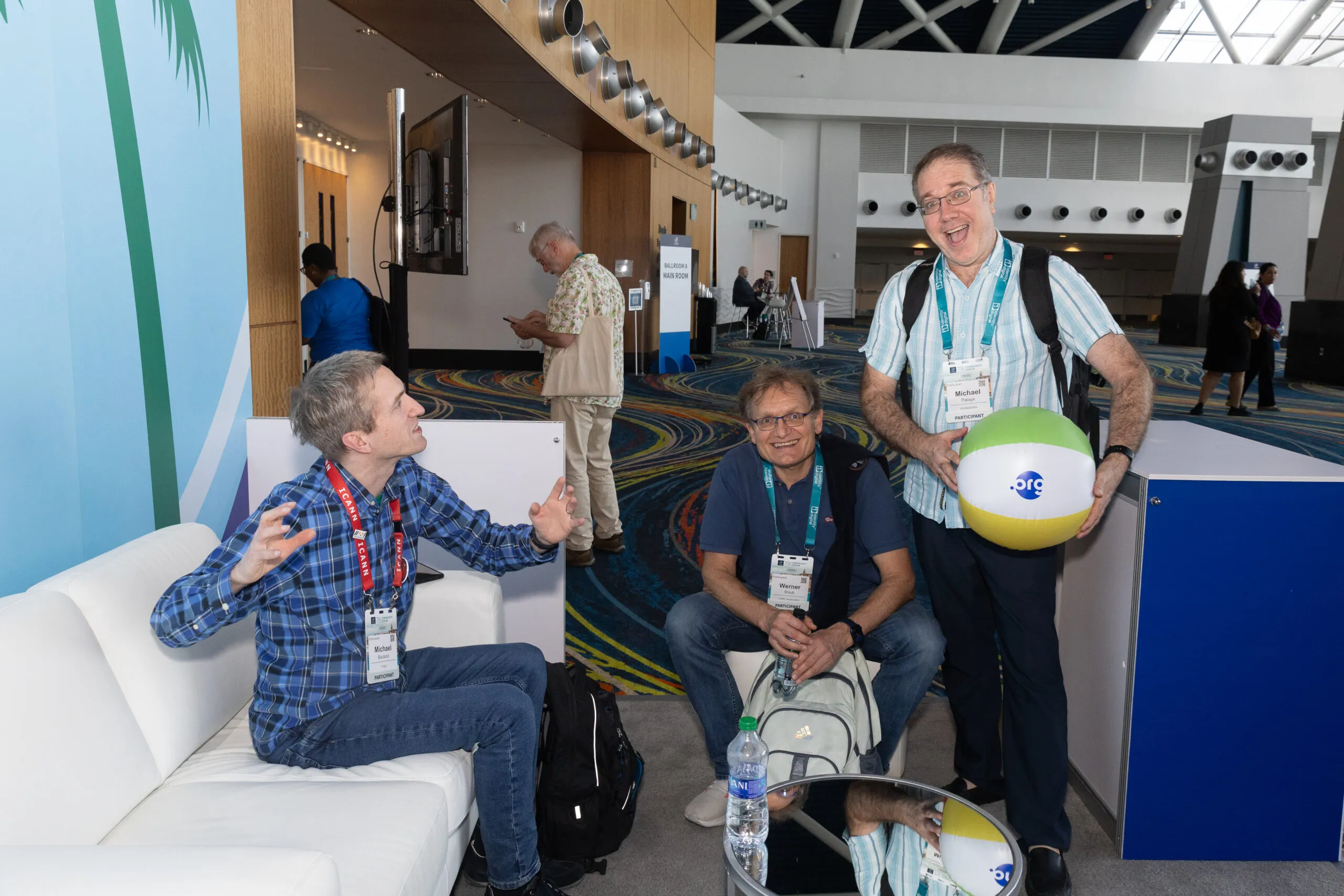 Three attendees chatting in a conference centre lobby, one holding a beach ball