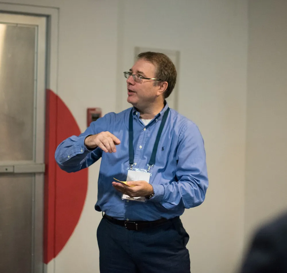 Speaker in a blue shirt and lanyard gesturing while presenting