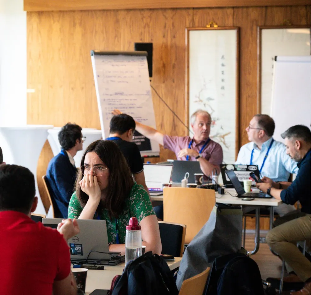 Workshop participants working on laptops around a table, with a flip chart behind them