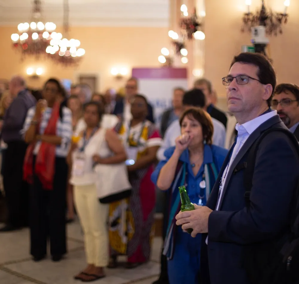 Attendees standing in a crowded reception hall under chandeliers