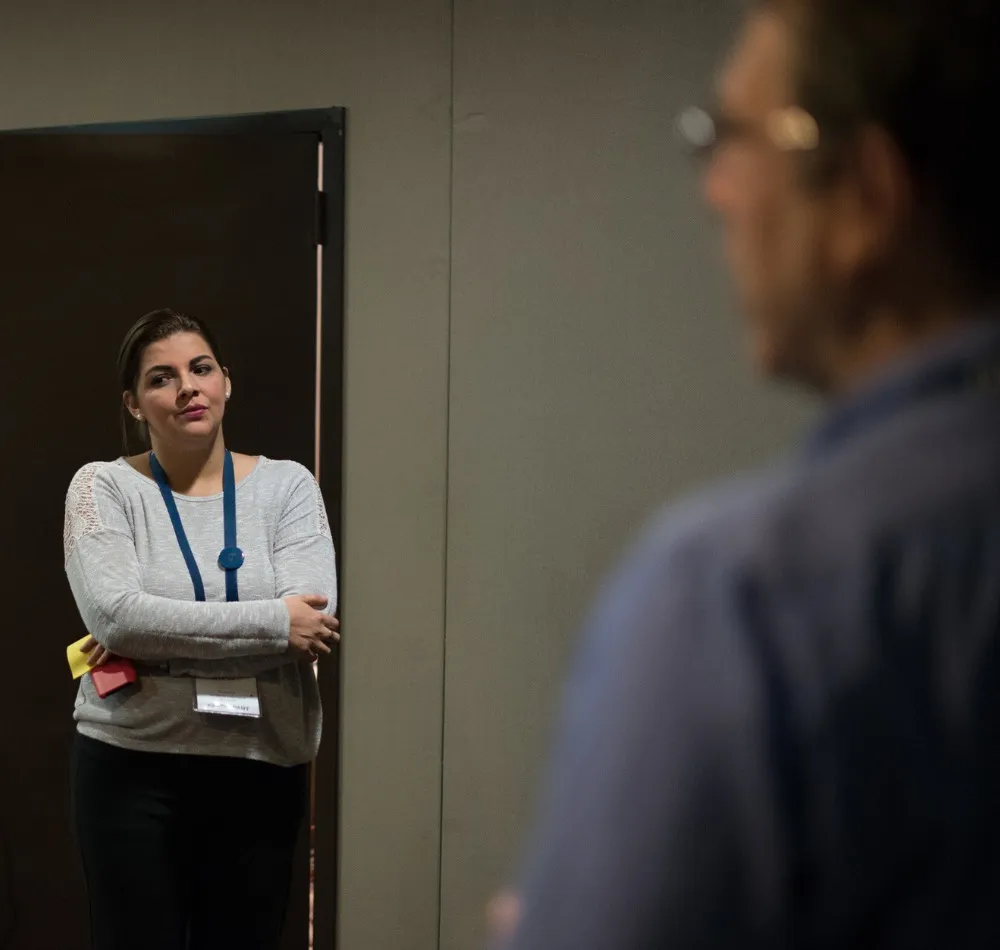 Meeting attendee with a lanyard listening, arms folded, by a doorway
