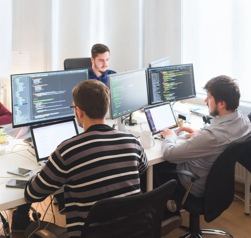 Developers writing code at desks with multiple monitors