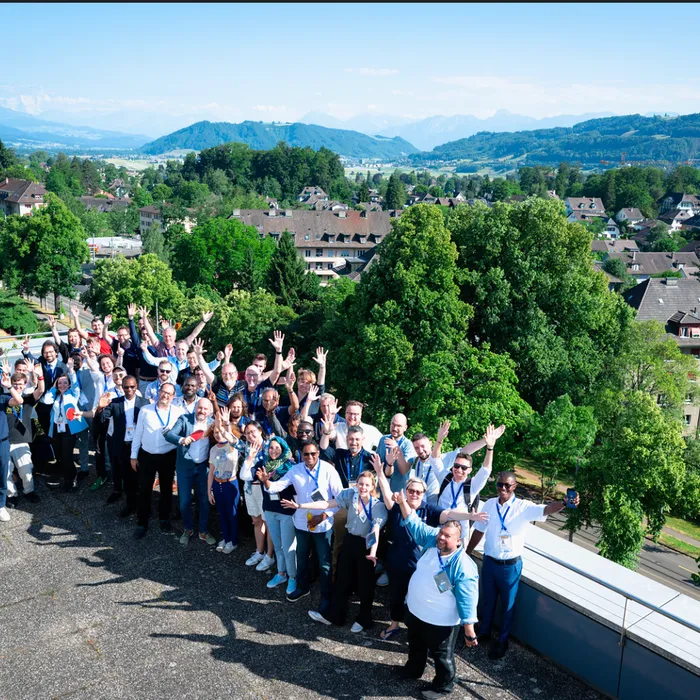 Hackathon participants waving in a group photo on a rooftop in Berne